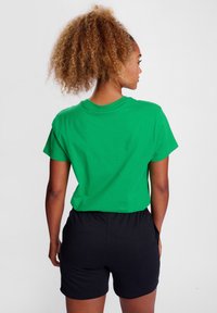 Zielona bawełniana koszulka z krótkim rękawem, luźny krój, w połączeniu z czarnymi szortami. Gładka tekstura, okrągły dekolt i prosty design.