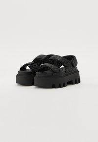Black platform sandals with crisscrossed quilted straps, thick rubber soles, and a chunky design. Smooth material with a textured appearance.