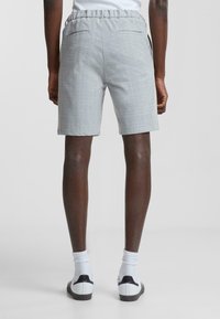 Pantalones cortos grises con un patrón, cinturilla elástica y dos bolsillos traseros, combinados con calcetines blancos y zapatillas negras y blancas.
