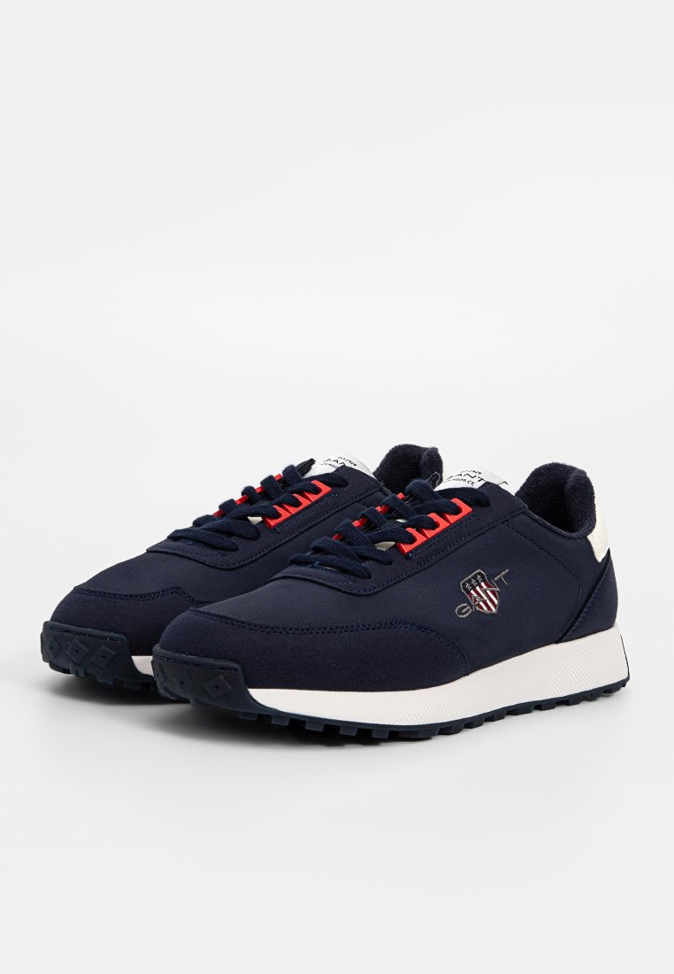 Mörkblå sneakers i tyg med en vit gummisula. Har röda detaljer på snörningen och logotypen. Rund tå med texturerat grepp.