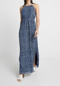 Maxiklänning i navy med blommönster i nyanser av blått och vitt. Har halterneck, elastisk midja och sidokluss.