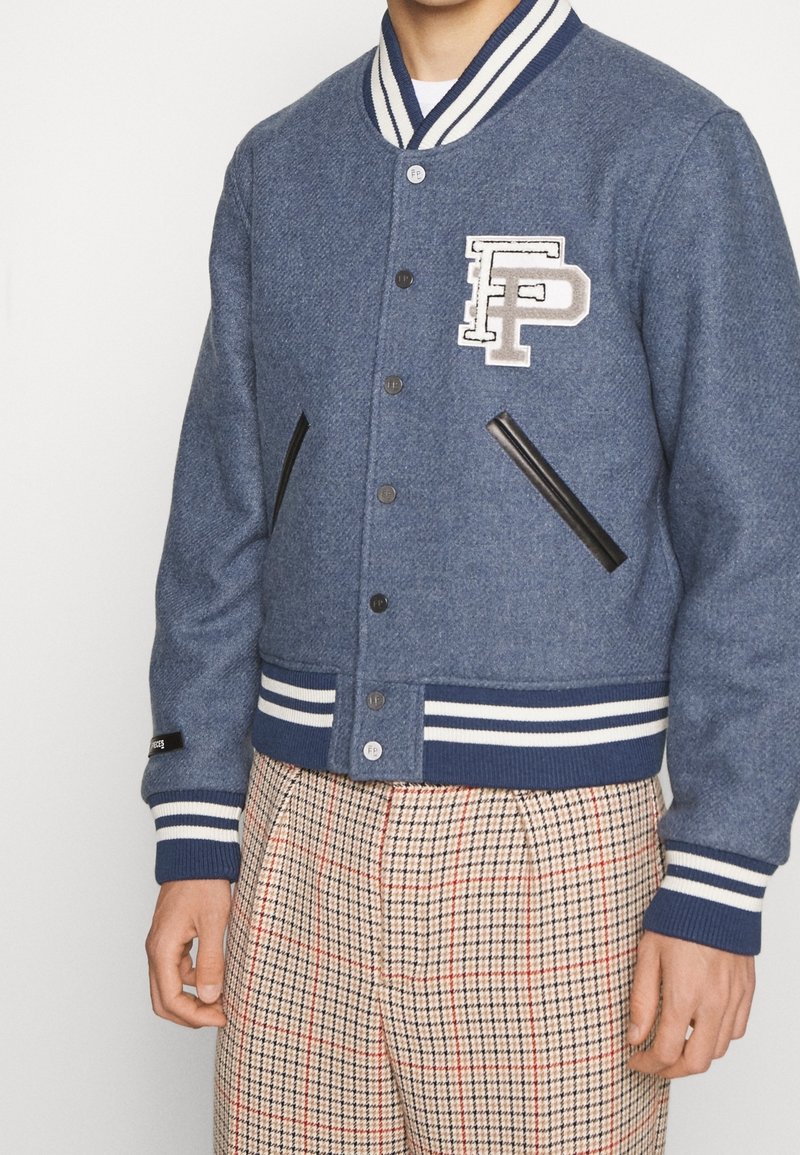 Blå varsityjacka i ullblandning med randig ribbad krage och muddar, med en framsides-logopatch och svarta fusk läder sidofickor.