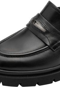 Κοντινό πλάνο μαύρου δερμάτινου loafers με παχιά ραβδωτή σόλα και μεταλλική διακοσμητική λεπτομέρεια σε σχήμα σταγόνας στο λουράκι πάνω.