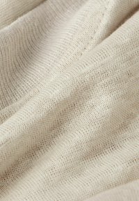 Světlé béžové texturované tkaniny, se jemným pleteným vzorem a měkkými vlákny, vykazujícími jemné barevné variace a hladký povrch.