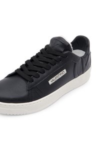 Černé kožené tenisky s černými tkaničkami, bílým vnitřním podšíváním a strukturovanými bočními panely. Obsahuje obdélníkovou logo nášivku na vnější straně.