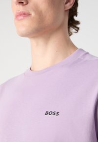 Sudadera de algodón morada con cuello redondo y un pequeño logotipo negro "BOSS" en el pecho. Textura suave, corte estándar.