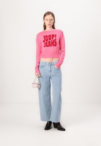 Fuchsia cropped sweater with "JOOP! JEANS" logo, light blue wide-leg jeans, black heeled ankle boots, and a small pink handbag.