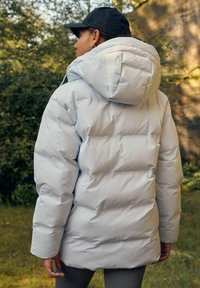 Lys grå pufferjakke med hætte, der har et quiltet design og elastiske manchetter. Blød tekstur, ideel til køligere vejr.