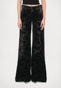 Črne žametne široke hlače z teksturiranim cvetličnim vzorcem, dvema sprednjima žepoma in zapiranjem na gumb v pasu.