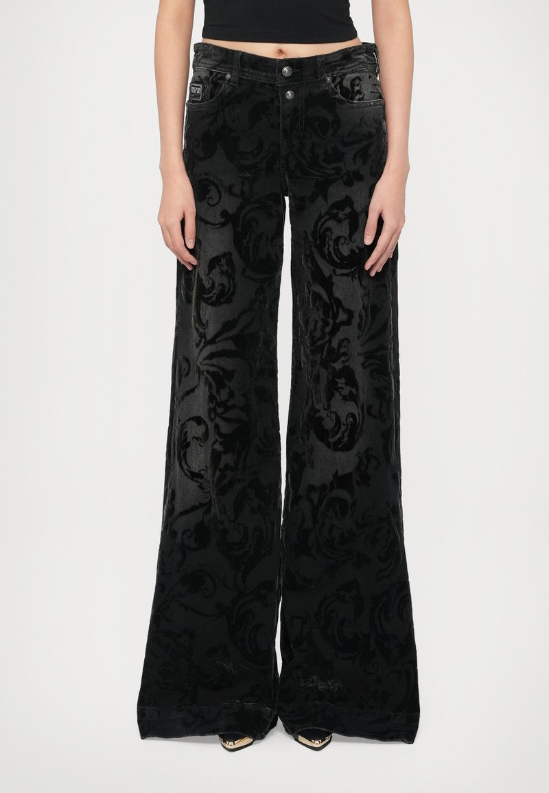 Črne žametne široke hlače z teksturiranim cvetličnim vzorcem, dvema sprednjima žepoma in zapiranjem na gumb v pasu.