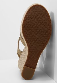 Beżowe sandały espadrille z plecionym materiałem, wklęsłym obcasem pokrytym jutą, gumową podeszwą z teksturowanym wzorem antypoślizgowym oraz otwartą piętą.