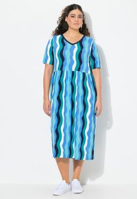 Vestido de manga corta y escote en V con un patrón de olas en varios tonos de azul, con un top ajustado y una falda suelta hasta la rodilla. Combinado con zapatillas blancas.