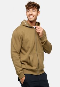 Khaki zip-up hoodie med blød tekstur, kengurulommer og hætte med snørredrag. Har branding på hættens foring. Casual pasform.