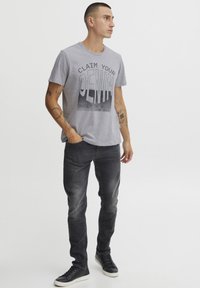 Grå bomull T-skjorte med svart tekst som sier "REKRUTTER DITT DENIM," kombinert med mørkegrå denimjeans og sorte sneakers. Enkelt design, avslappet passform.
