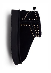 Bota de tobillo de ante negro con tachuelas doradas, suela plana de goma y una lengüeta en la parte trasera para facilitar su puesta. Superficie texturizada con acentos decorativos.
