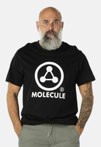 Čierne bavlnené tričko s veľkým bielym kruhovým logom s abstraktným dizajnom molekuly a slovom "MOLECULE" pod ním v tučných písmenách.