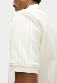 Hvid ribbet polo t-shirt med et tekstureret stof, der har en ombukket krave og korte ærmer. Minimalistisk design uden synlige logoer.