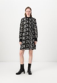 Vestido preto com padrão paisley branco, mangas longas, colarinho alto e punhos bordados, combinado com botas de tornozelo pretas brilhantes.