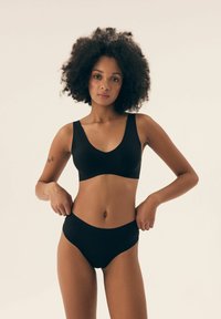 Czarny stanik i bikini o wysokim talii, oba wykonane z miękkiej, rozciągliwej tkaniny. Stanik ma szerokie ramiączka i okrągły dekolt.