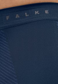 Ceinture en tissu extensible bleu avec le logo "FALKE", motif texturé, zone lisse et accents côtelés. Vue en gros plan des détails du matériau.