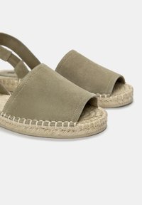 Suedetype espadrilles i dæmpet grøn med åbent tådesign, jute reb detaljer og flad sål. Justerbar bagside rem for sikker pasform.