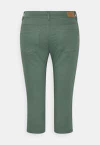 Vihreät lyhyet housut, valmistettu pehmeästä kankaasta, joissa on sileä pinta, kaksi takataskua ja ruskea nahkainen merkki vyötärönauhassa.