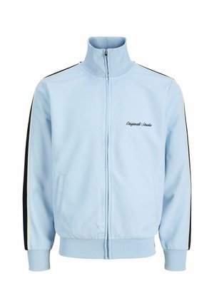 Hellblaue Trainingsjacke mit Reißverschluss, hohem Kragen, gerippten Bündchen und Saum, schwarz-weißen Streifen an den Ärmeln und dem Schriftzug „Originals Studio“ auf der Brust.