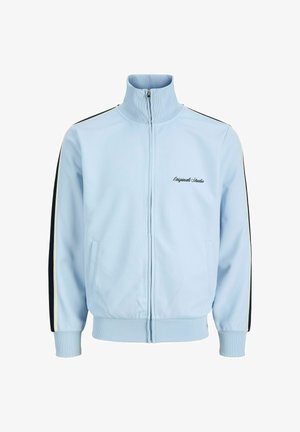 Hellblaue Trainingsjacke mit Reißverschluss, hohem Kragen, gerippten Bündchen und Saum, schwarz-weißen Streifen an den Ärmeln und dem Schriftzug „Originals Studio“ auf der Brust.