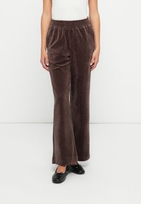 Zīda brūnas bikses ar plašu piegriezumu, elastīgu jostu un gludu tekstūru. Valkā ar melniem plakaniem apaviem kontrastam.