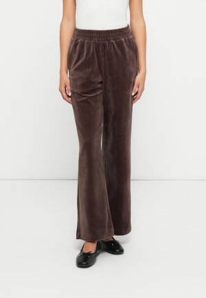 Braune Samthosen mit weitem Beinschnitt, elastischem Bund und glatter Textur. Getragen mit schwarzen flachen Schuhen für den Kontrast.