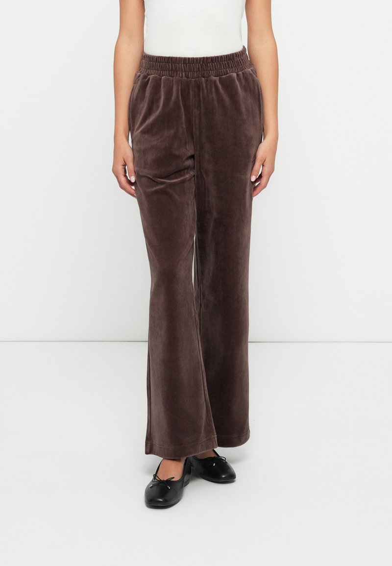 Zīda brūnas bikses ar plašu piegriezumu, elastīgu jostu un gludu tekstūru. Valkā ar melniem plakaniem apaviem kontrastam.