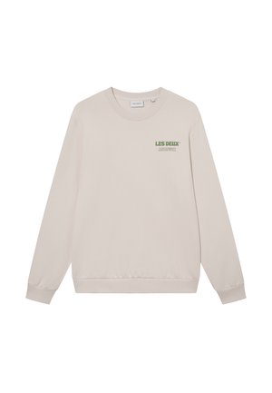 Šviesiai rudas džemperis, pagamintas iš minkštos medžiagos, su apvaliu kaklu, raukiniais ant rankovių ir žaliai spausdintu logotipu ant krūtinės. Paprastas, laisvas dizainas.