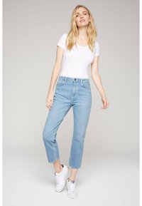 Jeans de tiro alto en azul claro con corte recto, que cuentan con cierre de botón y cinco bolsillos. Combinados con una camiseta blanca ajustada y zapatillas blancas.