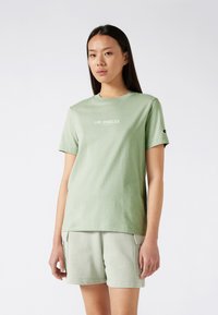 Camiseta de algodón verde claro con cuello redondo, mangas cortas, texto "LOS ÁNGELES" en blanco y detalle del logo en la manga; combinada con pantalones cortos a juego.
