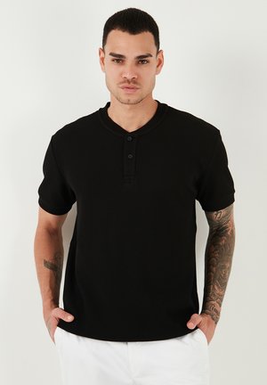 Camiseta henley de manga corta negra con cuello en V y tapeta de tres botones, que presenta aberturas laterales y una tela texturizada.