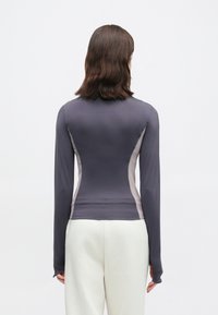 Μπλούζα με μακριά μανίκια σε σκούρο γκρι χρώμα με ανοιχτό γκρι πλαϊνές ραφές. Λείο ύφασμα, στρογγυλή λαιμόκοψη και άνοιγμα στους καρπούς σχεδιασμένα για αθλητική εφαρμογή.