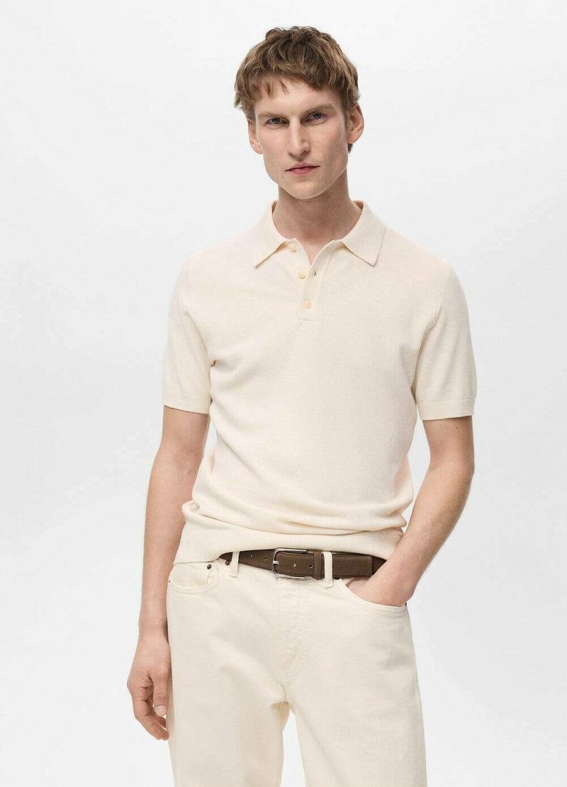 Polo cu mânecă scurtă de culoare crem, dintr-un material texturat, cu o închidere cu trei nasturi și o guler clasic, asortat cu pantaloni de culoare deschisă și o curea maro.