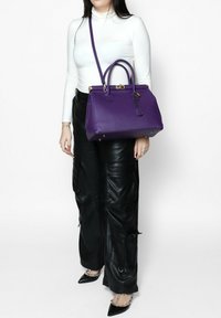 Borsa a tracolla in pelle viola con due manici superiori, hardware dorato e una tracolla rimovibile. Superficie testurizzata con un design strutturato.