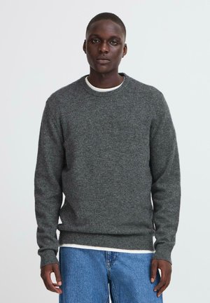 Grau gestrickter Pullover mit rundem Halsausschnitt und gerippten Bündchen, über einem weißen Hemd getragen, kombiniert mit blauen Jeans.