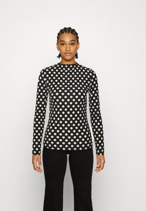 Blusa de mangas compridas ajustada em preto com bolinhas brancas, textura canelada e decote alto. Combinada com calças flare pretas.