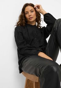 Black textured blouse featuring wavy patterns, button closure, and gathered sleeves, paired with black faux leather pants.