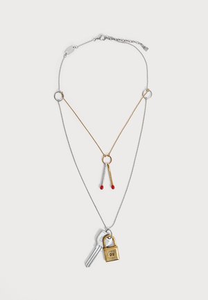 Zwei lagige Halsketten mit Silberketten, eine mit einem goldenen Ring und zwei Streichholz-Anhängern, die andere mit einem Schlüssel und einem kleinen goldenen Vorhängeschloss.