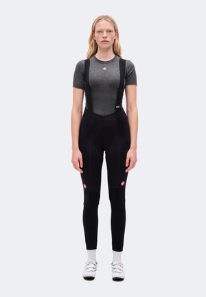 Un mannequin se tient devant un fond uni, vêtu d’un maillot de cyclisme gris, d’un cuissard long noir à bretelles, de chaussettes blanches et de chaussures de cyclisme blanches.
