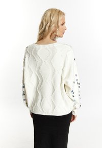 Pulover alb supradimensionat din tricot, cu model texturat în zigzag și paiete colorate pe mâneci. Guler și manșete ribburate, croială lejeră.