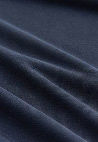 Gros plan d’un tissu bleu foncé avec une texture finement côtelée et des plis doux créant des ombres légères.