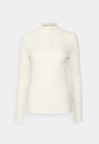 Pitkähiha, ribbattu paita luonnonvalkoisena. Sisältää korkean kauluksen ja viiden napin halkion. Valmistettu pehmeästä, joustavasta kankaasta.