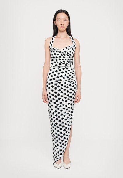 Schwarz-weißer Pünktchenkleid mit Halterhals, gerafftem Design, bodenlang und mit einem seitlichen Schlitz. Glattes Gewebe mit leichtem Glanz.