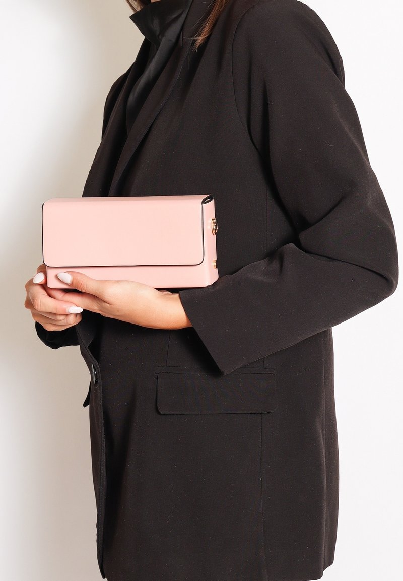 Clutch rettangolare rosa con una texture liscia, bordi neri e una chiusura dorata, tenuto in mano davanti a uno sfondo di giacca nera.