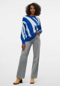 Pull en maille rayé bleu et blanc à manches longues, col rond, coupe décontractée, associé à un jean gris à jambes larges et des bottines à talons marron clair.