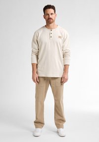 Lichtbeige langermige shirt met een henley-halslijn en drie knopen, gecombineerd met beige cargobroek en witte sneakers. Eenvoudig ontwerp en pasvorm.